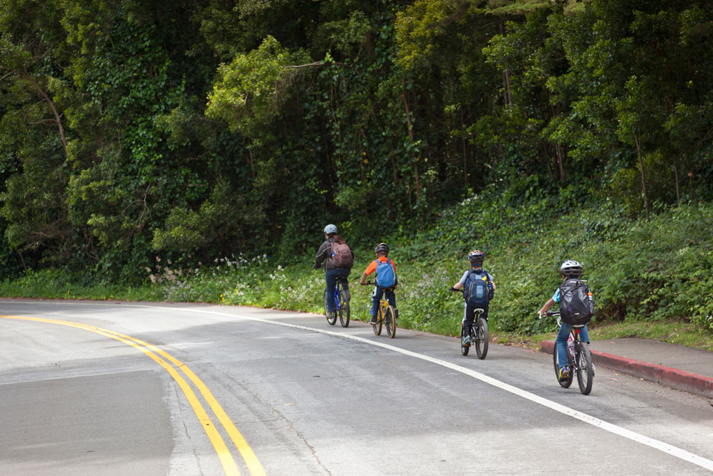 Adult and three kids riding bikes down bike path on road