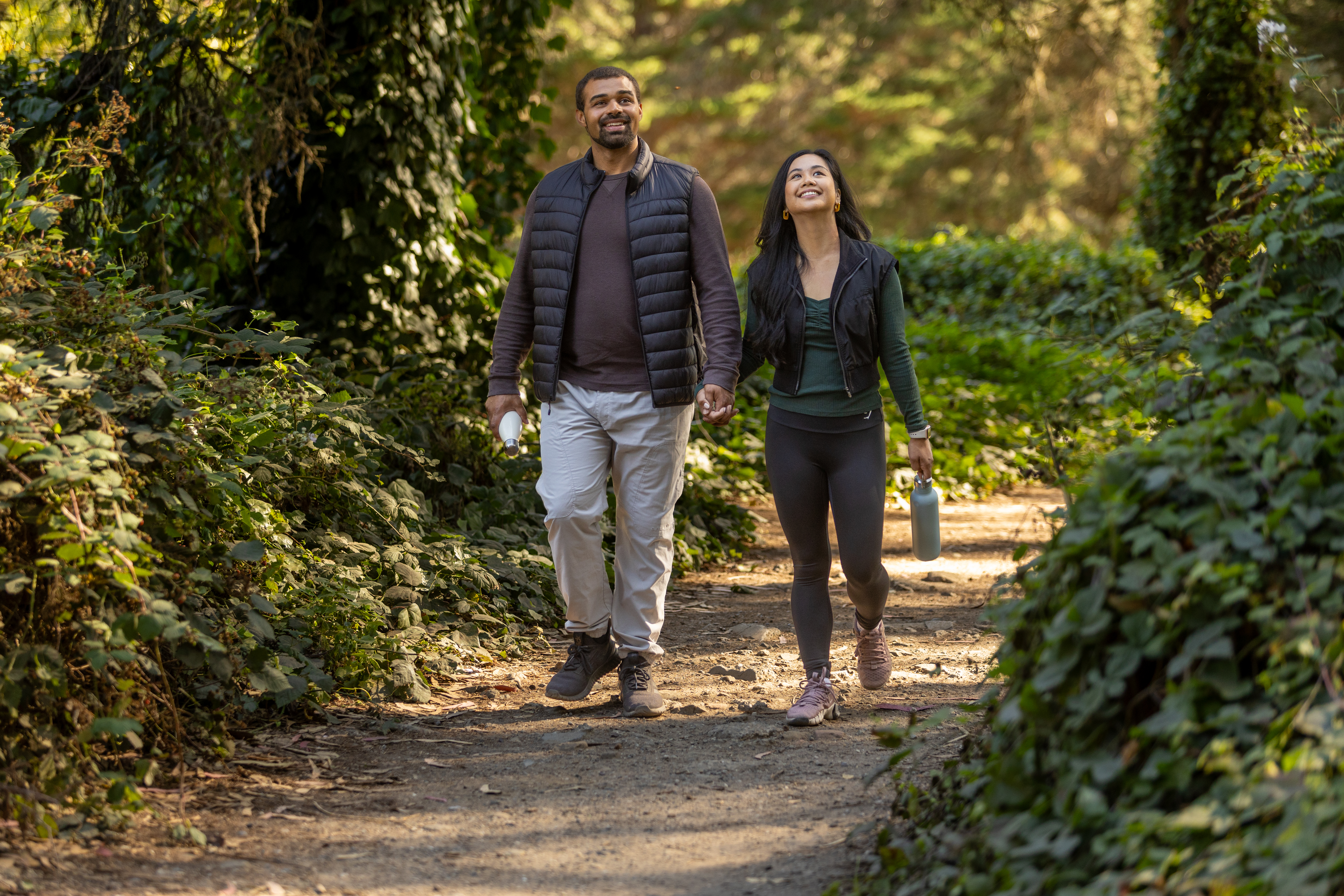 Couple holding hands and walking through the woods in the Presidio