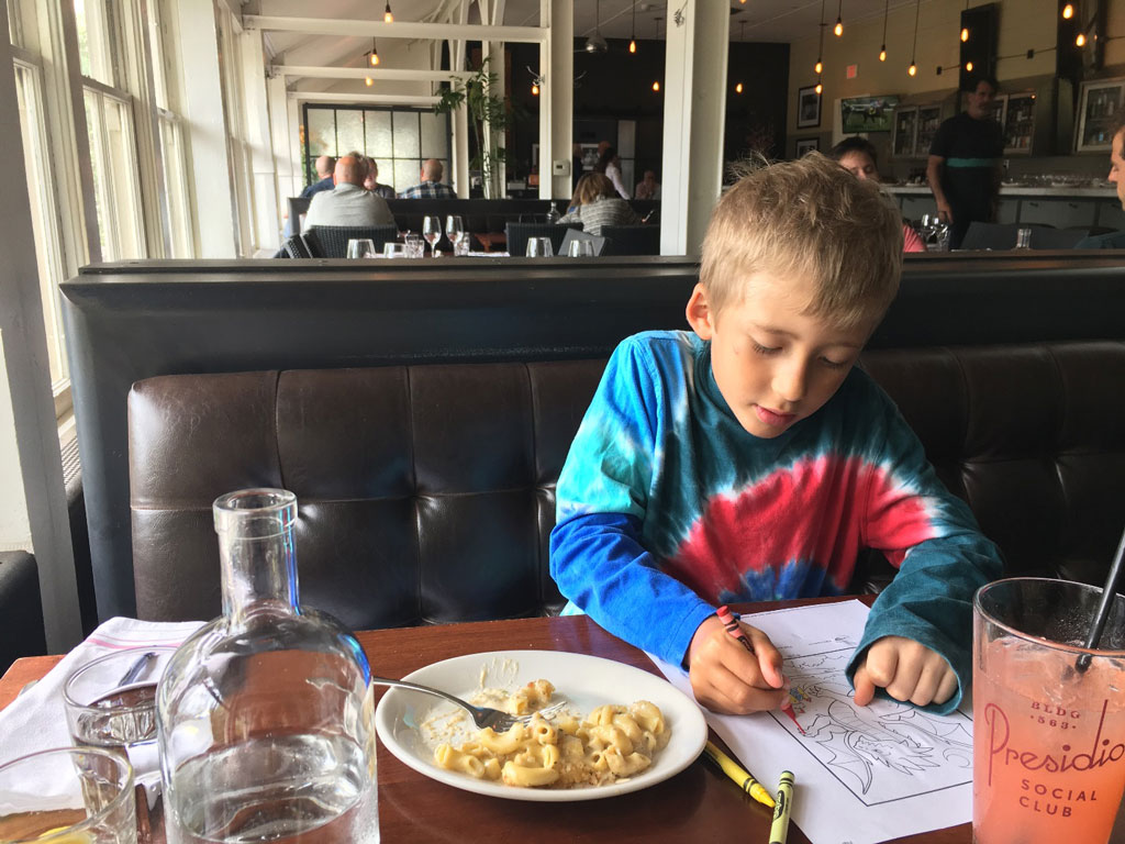 Child coloring next to plate of mac and cheese