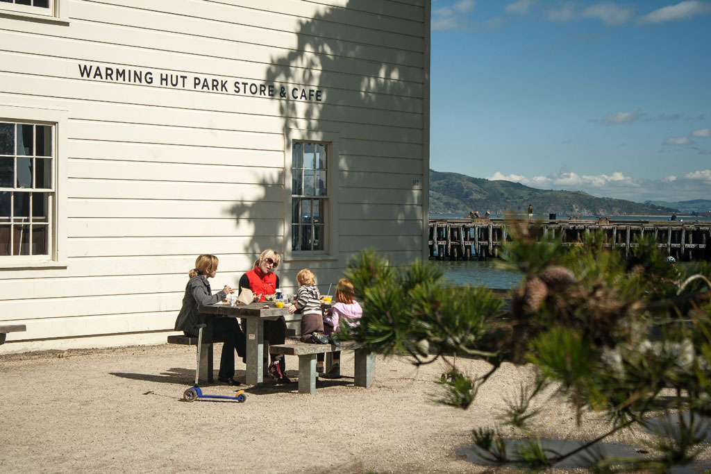 Adults and kids at picnic table next to Warming Hut with Torpedo Wharf view