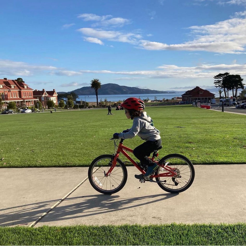 Child in helmet biking on  sidewalk at Main Parade Lawn