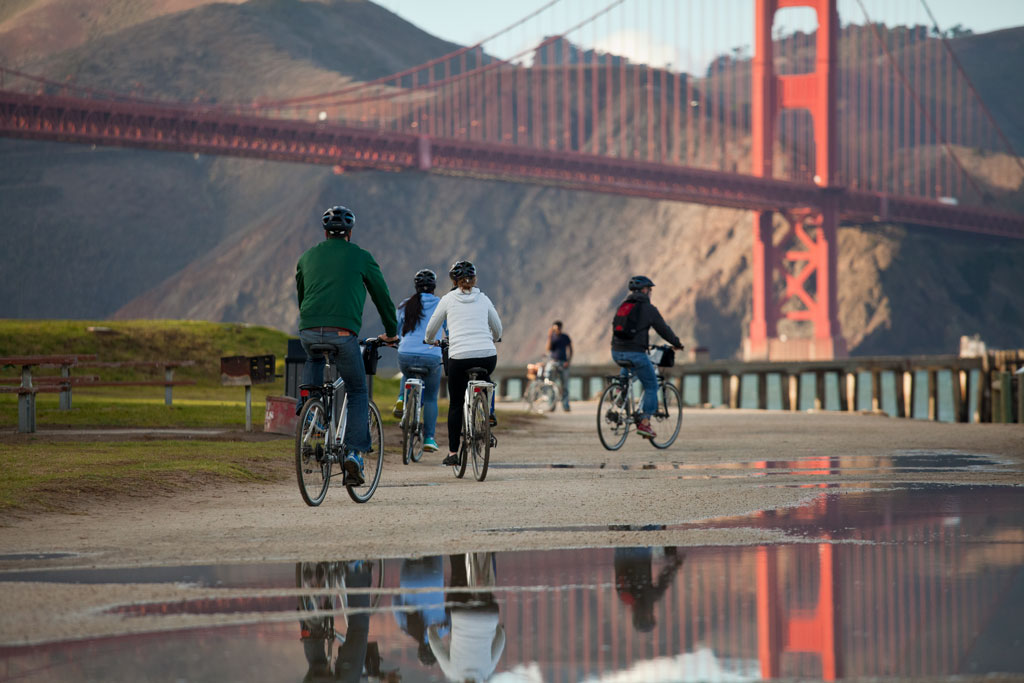 Bicyclists riding on dirt path towards Golden Gate Bridge