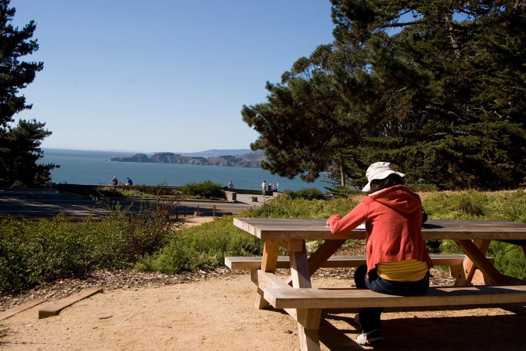 Visitor in red sitting at picnic table and facing towards bay view