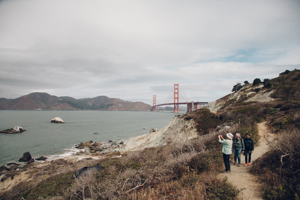 Visitors on trail and taking a photo into the bay. Golden Gate Bridge is seen in the background.