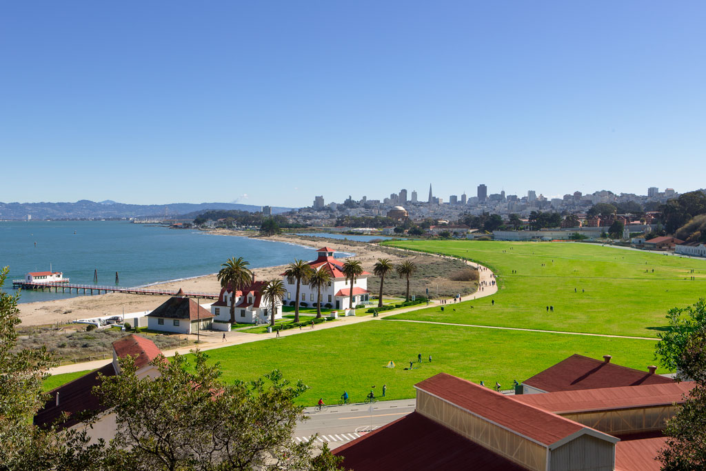 View of Crissy Field lawn, buildings, bay, and San Francisco city skyline.