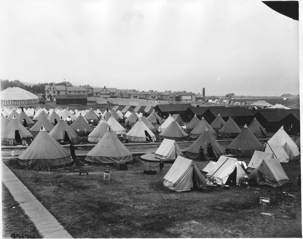 Relief camp tents lined with circus tent and buildings in the background