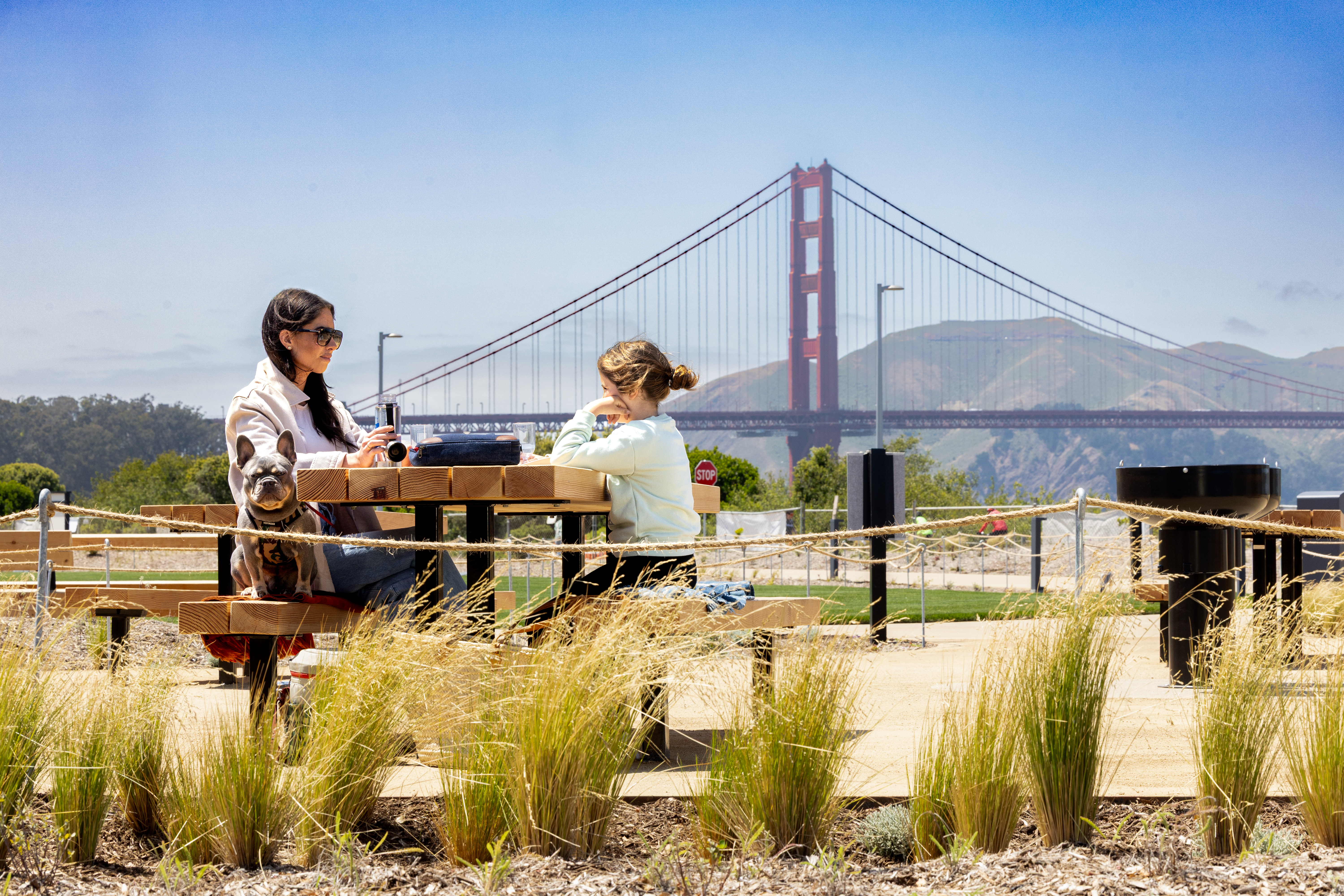 Mother and daughter sitting at picnic table at the Outpost Meadow Picnic Area with the Golden Gate Bridge in the background