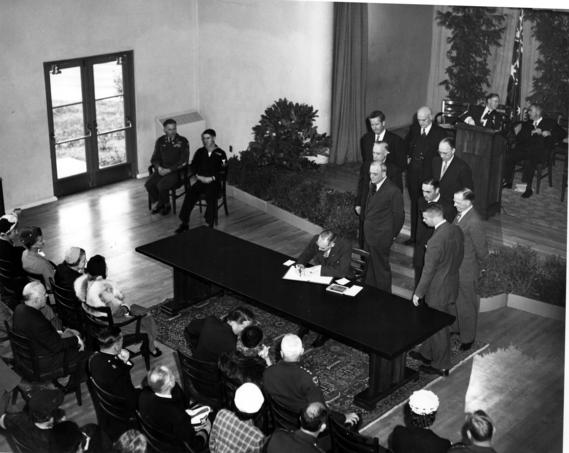 Secretary of State Dean Acheson signing ANZUS treaty in front of witnesses and audience.