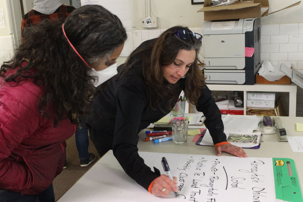 Woman writing on big Post It notepad with another woman standing over looking.