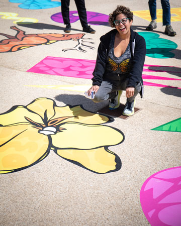 Favianna smiling while kneeled next to yellow flower art