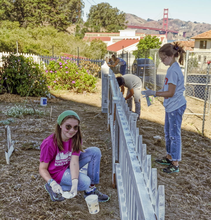 Three kids volunteer to paint the fence at Presidio Pet Cemetery.