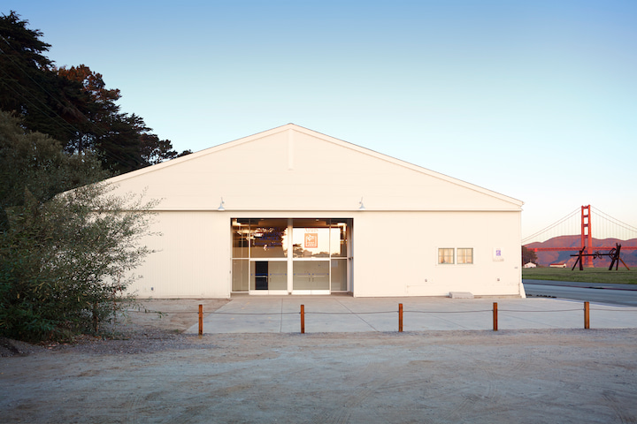The exterior of the center at Crissy Field, with the Golden Gate Bridge in the background.