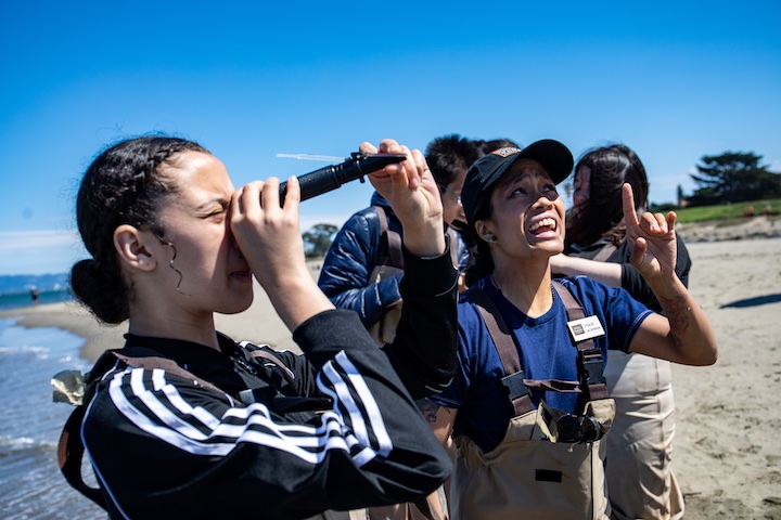 A group of teenagers look through a telescope. Photo by Paul Myers.