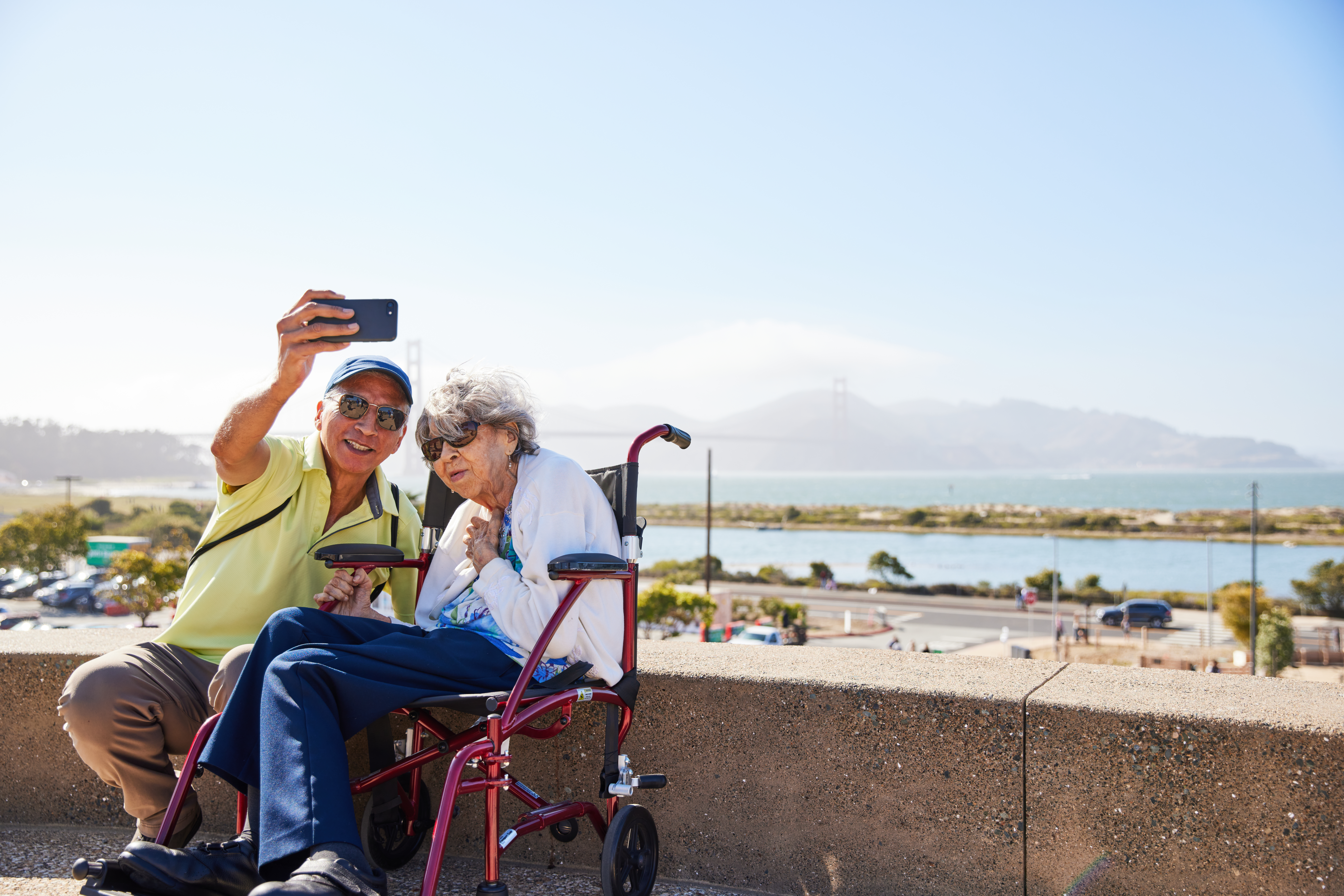 Man and elderly woman taking a selfie on the Presidio Tunnel Tops with the Golden Gate Bridge in the background.