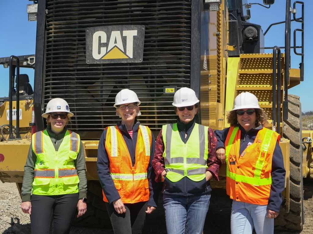 Group of four women in construction gear standing in front of a CAT tractor. From left to right: Lauren Connolly, Teddy Huddleston, Paula Cabot, Rania Rayes