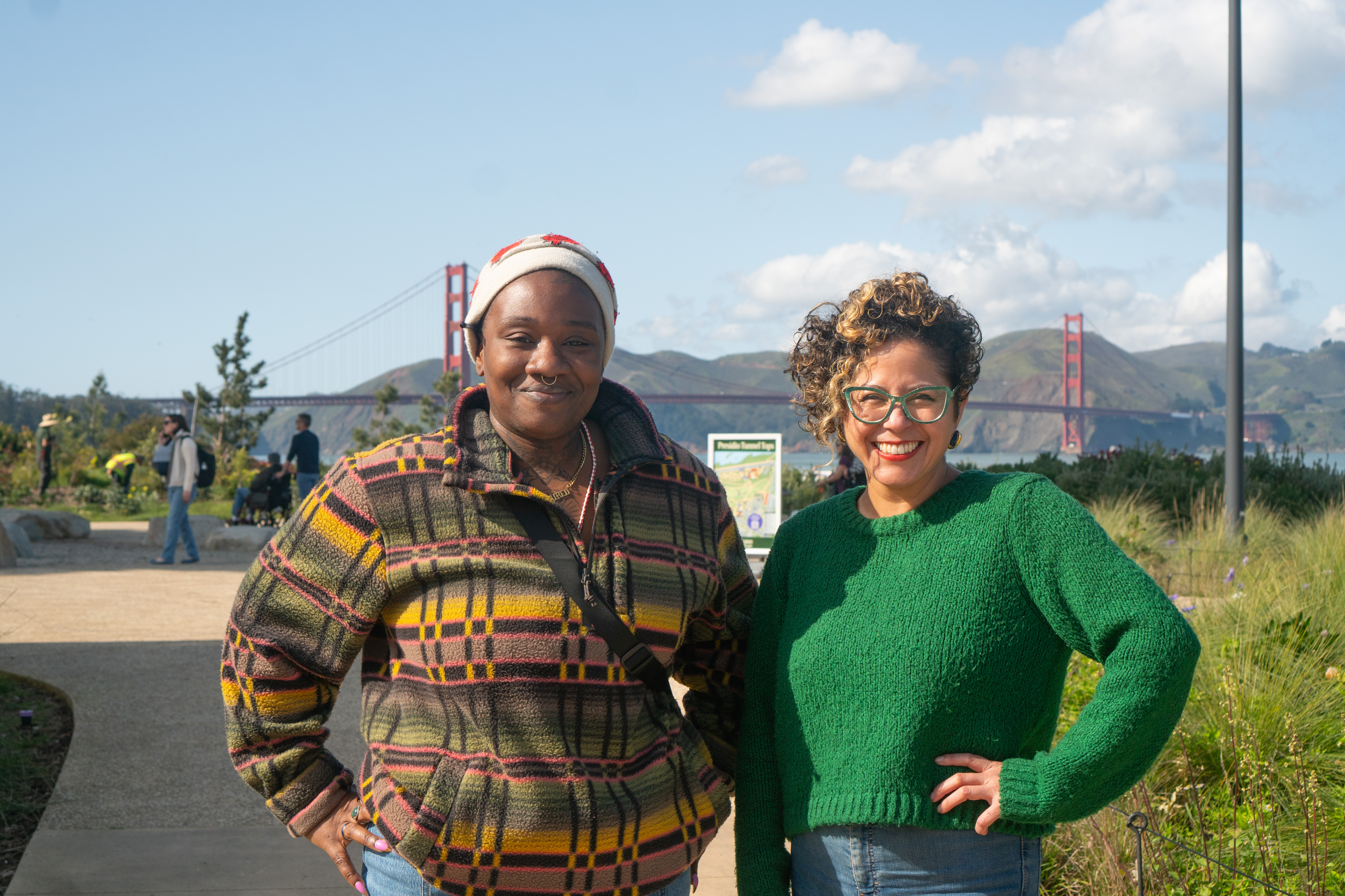 Two women, Tosha and Artist and Presidio Activator Favianna Rodriguez, standing and smiling on the Presidio Tunnel Tops with the Golden Gate Bridge in the background.