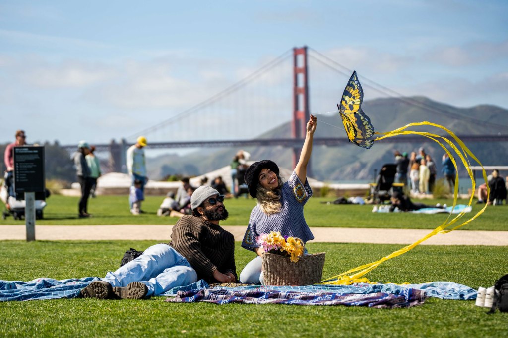 Couple visitors on picnic blanket flying low kite at a Presidio Tunnel Tops lawn