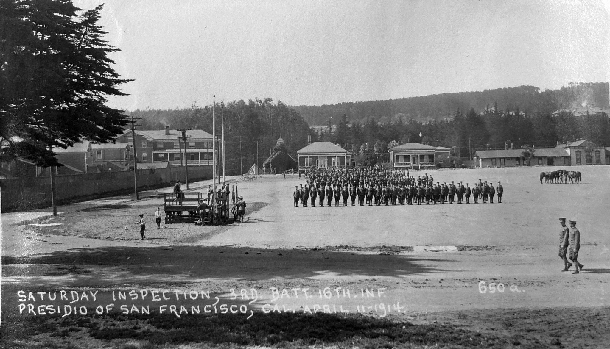 External black and white photo of the Main parade lawn with troops on the parade ground with the barracks in the background,