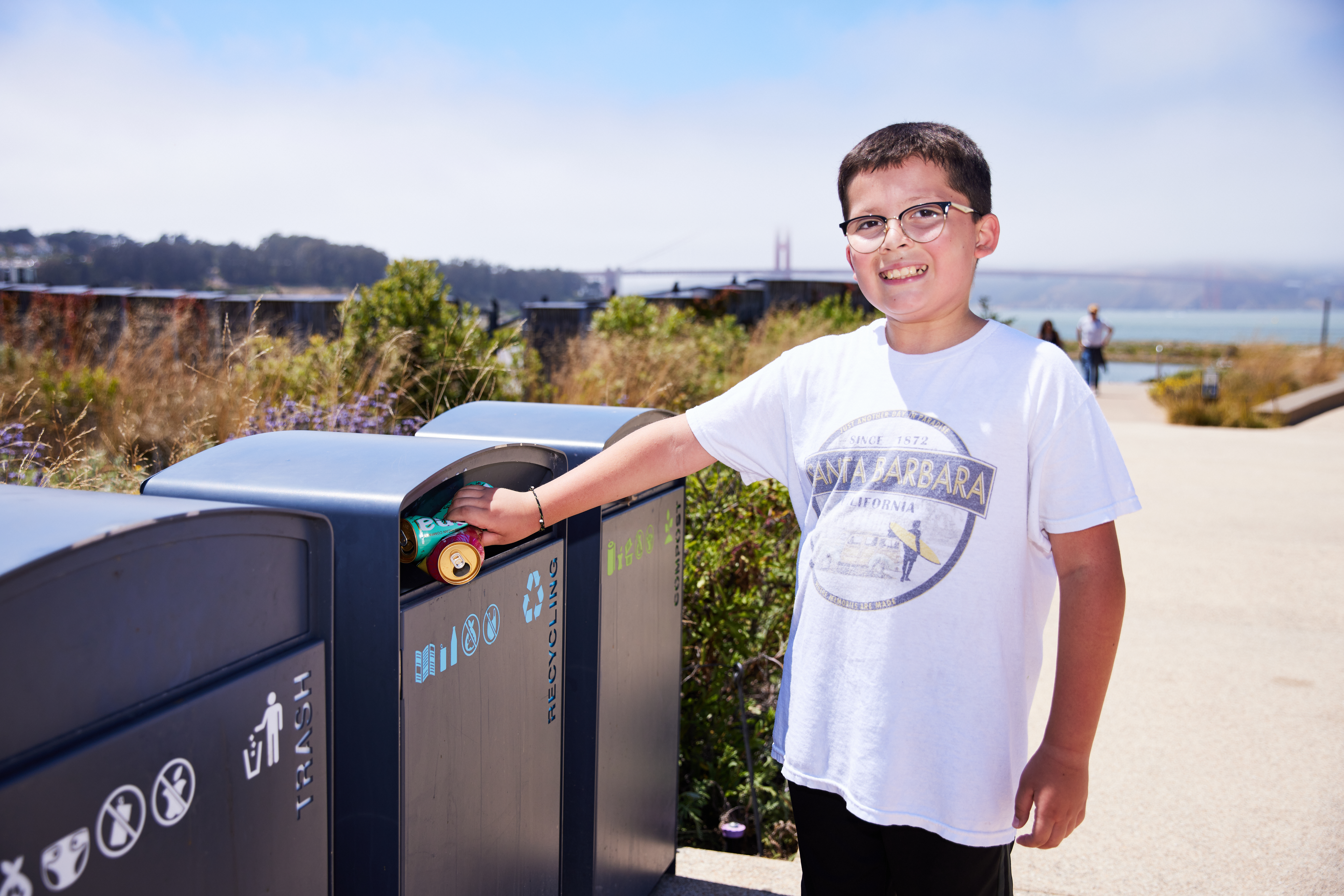 A young boy demonstrating how to recycle properly on the Presidio Tunnel Tops with the Golden Gate Bridge in the background