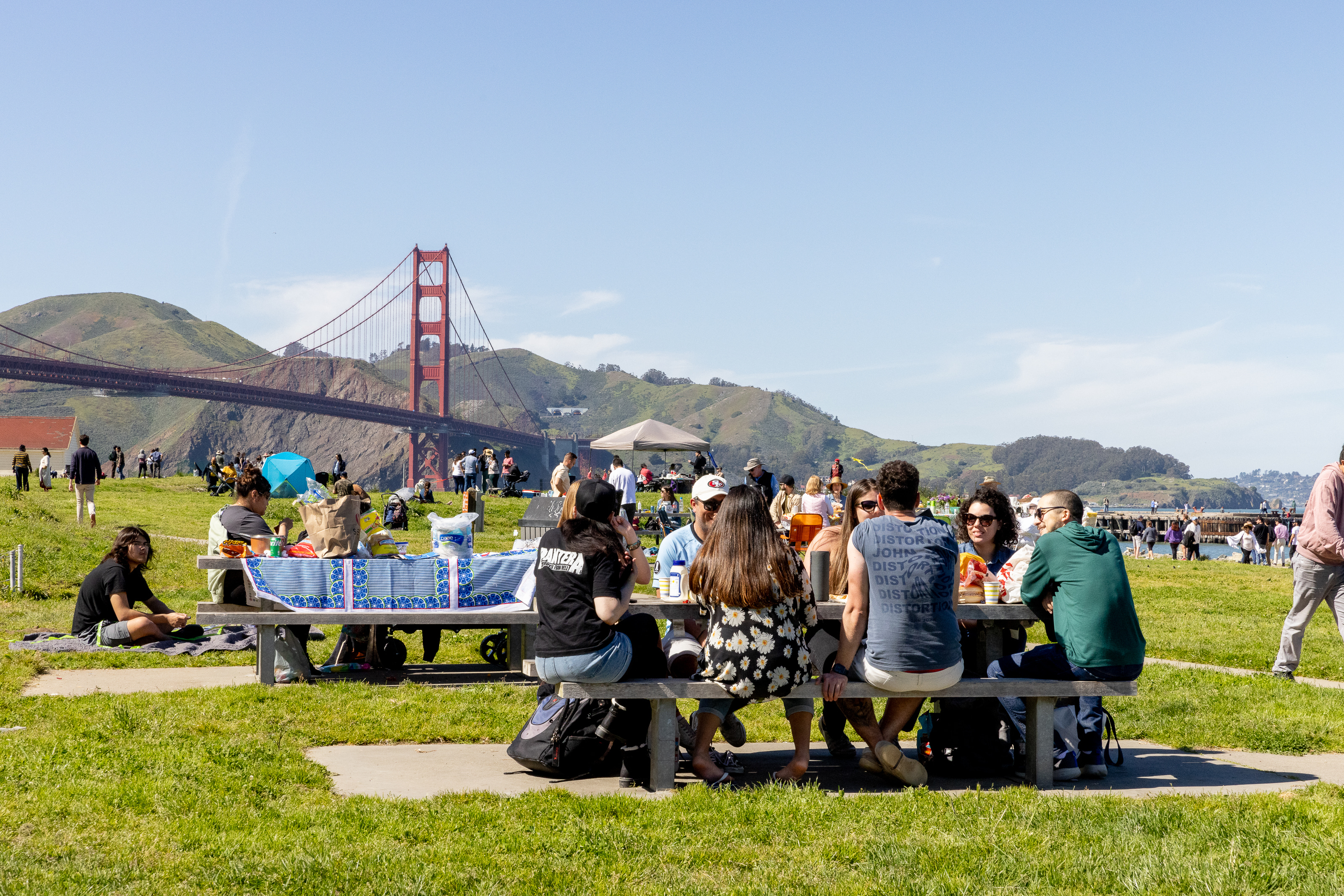 A group of people picnicking at Crissy Field on a sunny day with the Golden Gate Bridge in the background