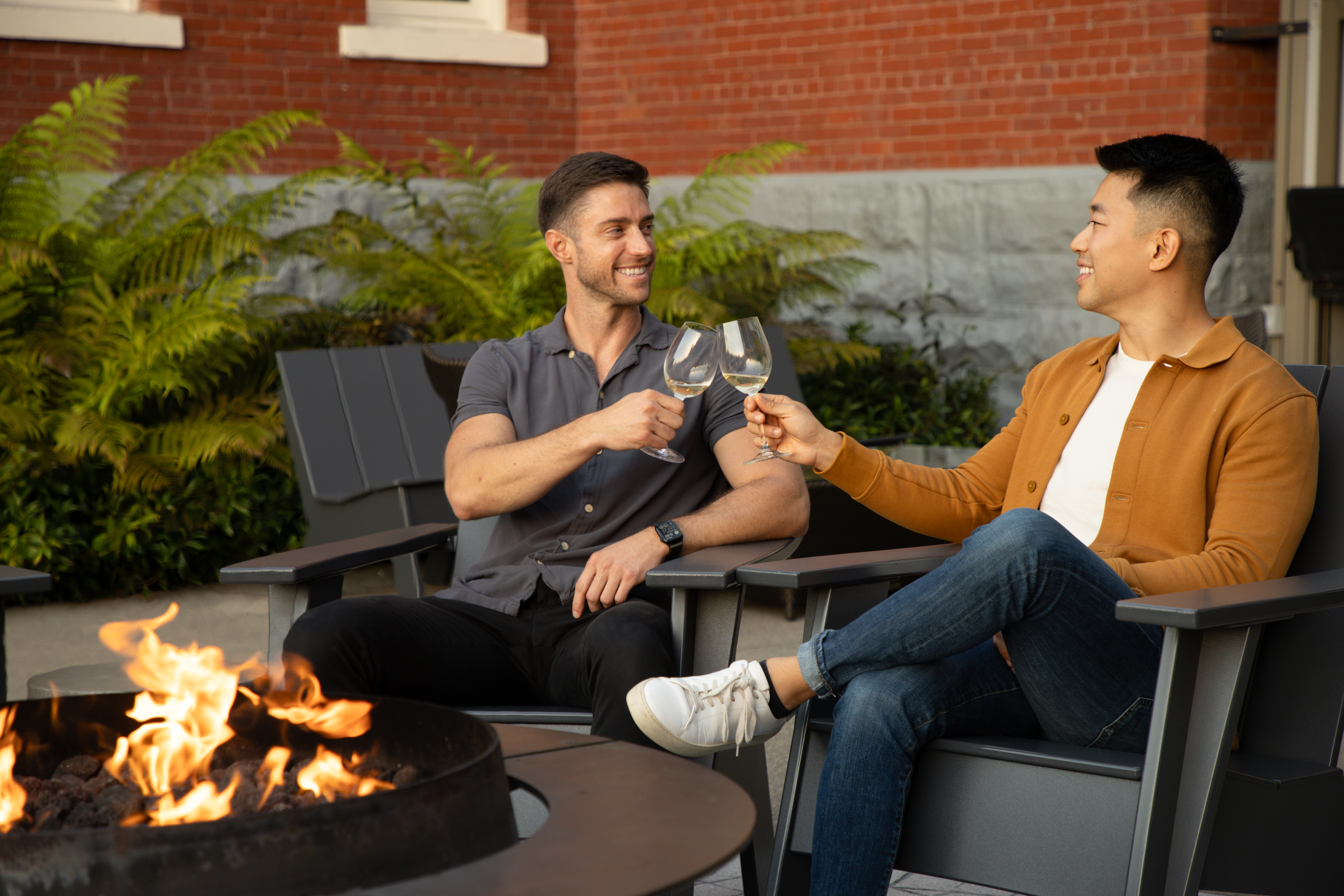 Two men happily cheering wine glasses by a fire