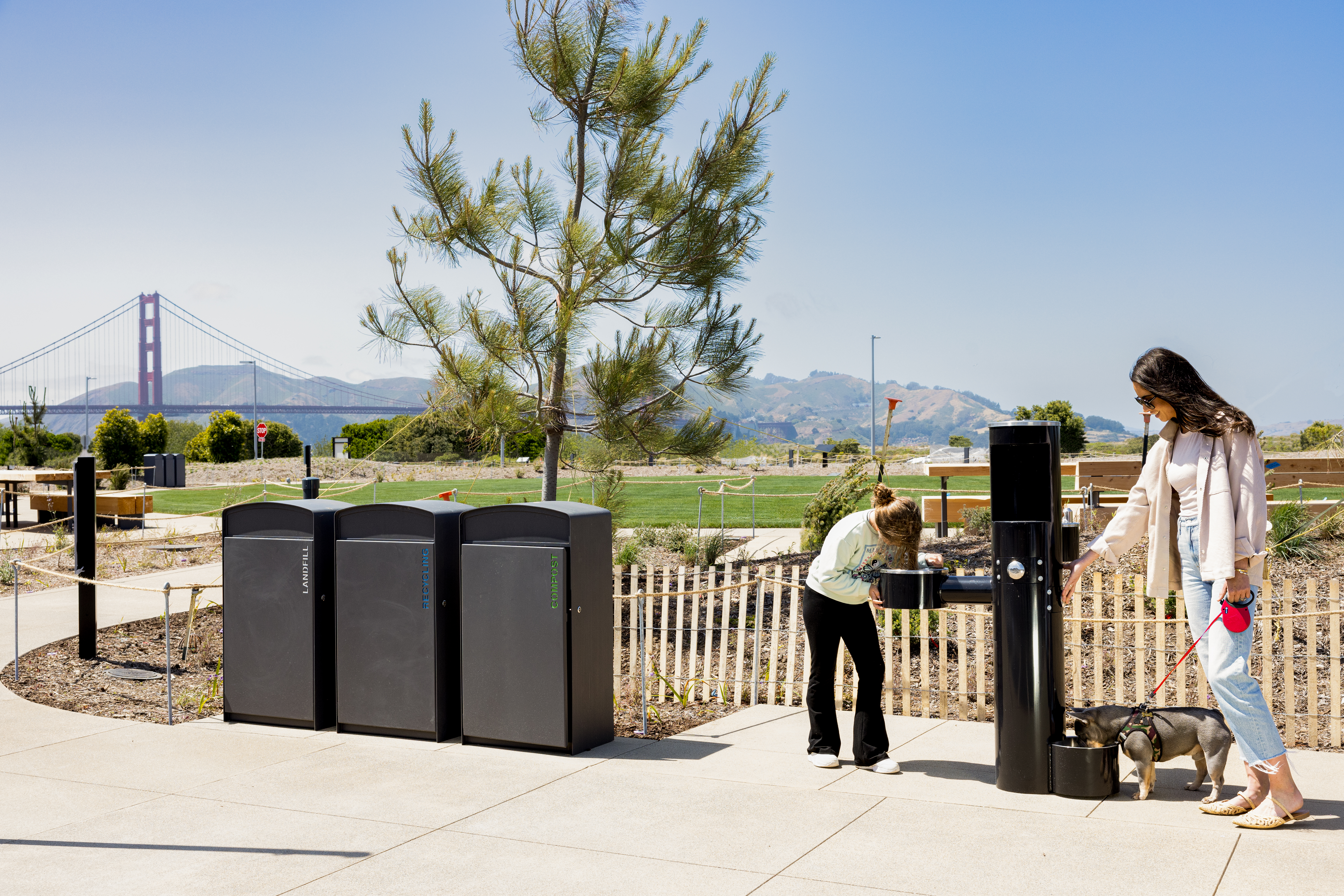 Woman, girl, and dog use a water fountain at the Outpost Meadow picnic area at Presidio Tunnel Tops.