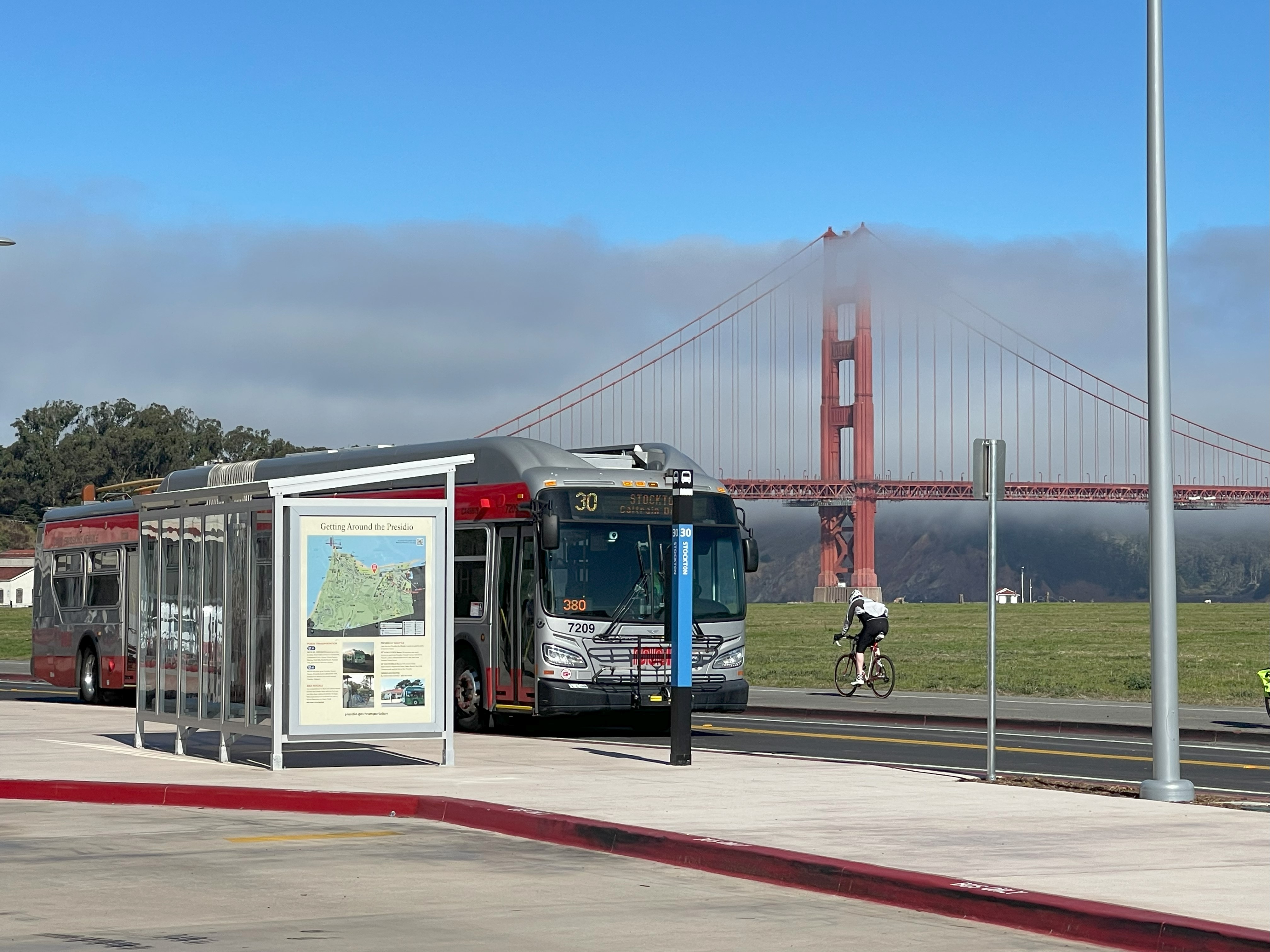 Muni 30 driving on Mason St with a bike riding past in the opposite direction and the golden gate bridge in the background