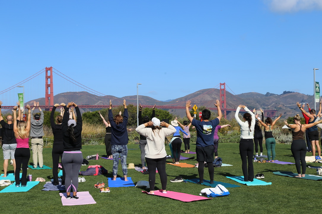 People practicing yoga at the Outpost Meadow with the Golden Gate Bridge in the background