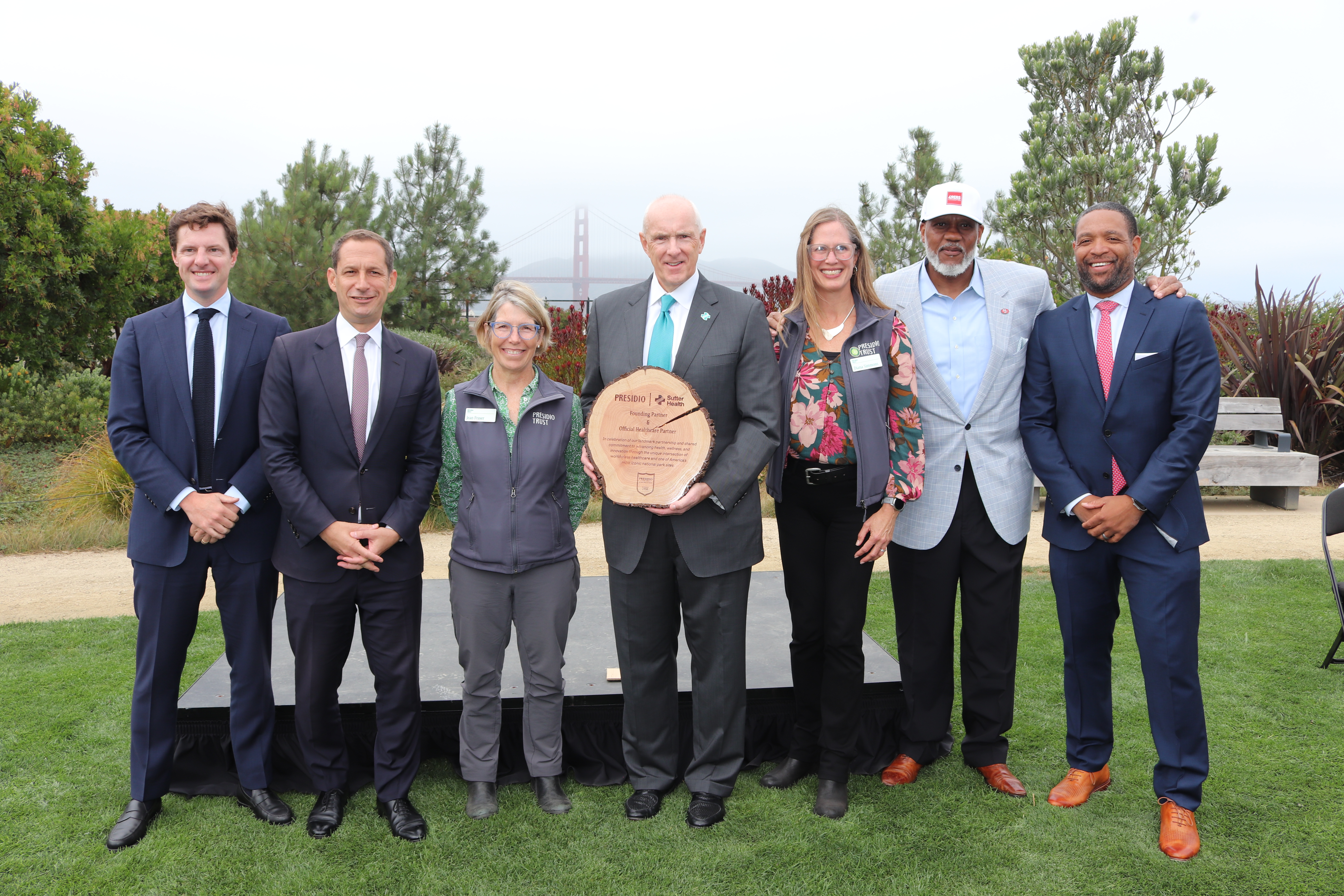City officials and Sutter Health and Presidio Trust executives standing at the podium with the Golden Gate Bridge in the background.
